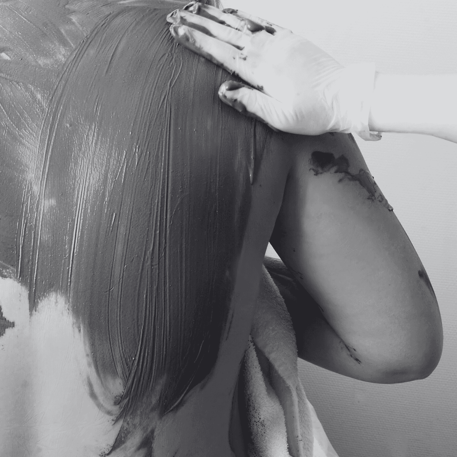 Person receiving a therapeutic mud treatment on their back, close-up of hands applying mud.